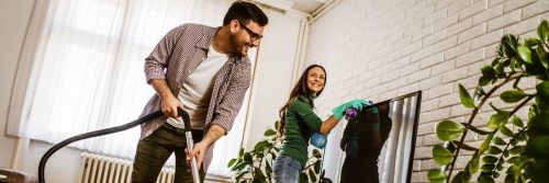 couple happily does household chores together vacuuming floor wiping mirror