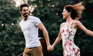 couple holds hands smiling walking near forest