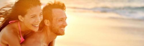 man carries girlfriend on back walking on beach in sunny sky