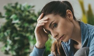 woman hand on forehead sitting on couch thinking