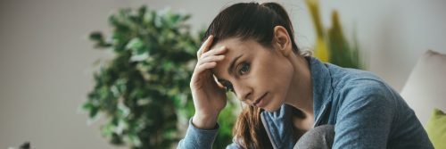woman hand on forehead sitting on couch thinking
