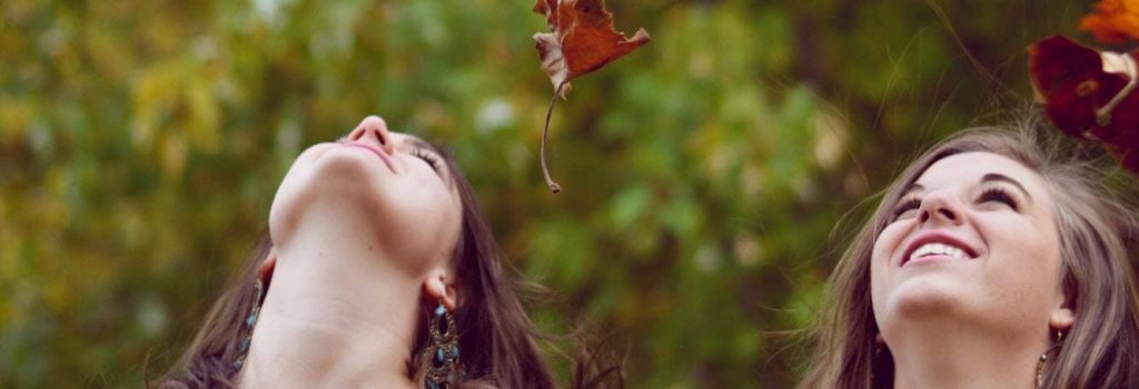 two women happily look at beautiful sky red leaves flying