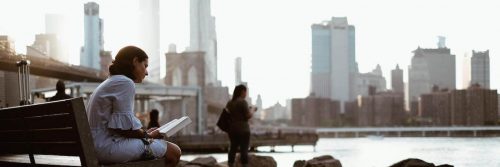 woman sits alone bench on seaport reading book