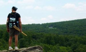 man standing on rock looking green forest in peaceful cloudy sky