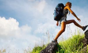 man wearing large blue back bag walks on rock in blue cloudy sky