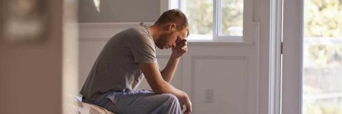 man sits on bed hand in face sadly thinking during challenging period