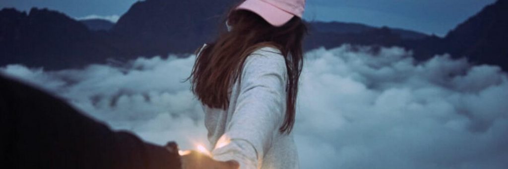 woman facing backward wearing pink cap holding partner hand walking in cloudy sky