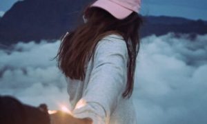 woman facing backward wearing pink cap holding partner hand walking in cloudy sky