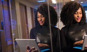 curly hair woman carrying laptop stands next to wall in office