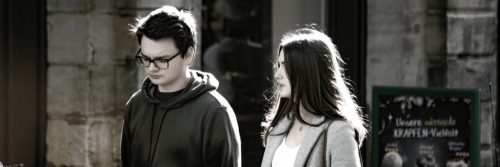 couple walks along street talking beside old building while man feeling tired angry