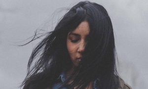 woman stands eyes closed sadly thinking in cloudy sky
