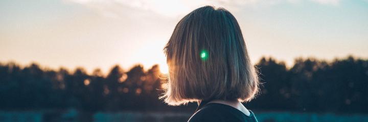 short hair woman stands in forest looking at sunset