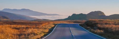 empty road approaching mountain between fields in cloudy sky