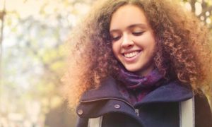 curly blonde hair woman looks down happily smiling next to fence in sunny sky