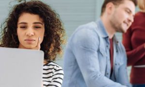 girl looking at laptop thinking while two colleges discussing pointing at laptop