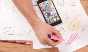 hand using pink highlighter highlighting sentence on paper mindmap table beside iphone pencil case