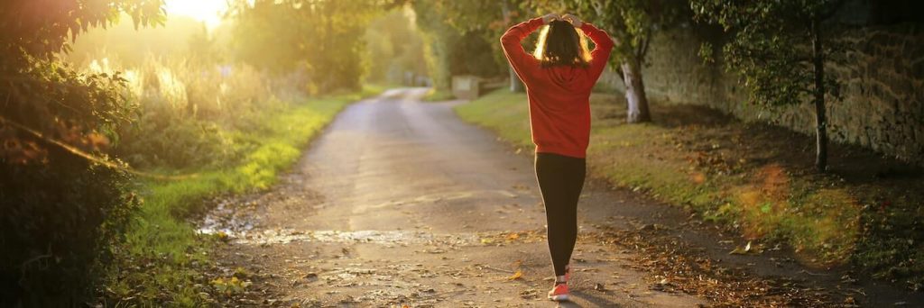 woman hands on hair walked along footpath between bushes in beautiful sunny weather