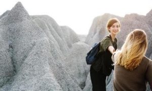 two women climb rocks in shining sky