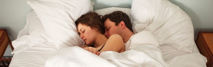 couple sleeps tightly on bed beside side table