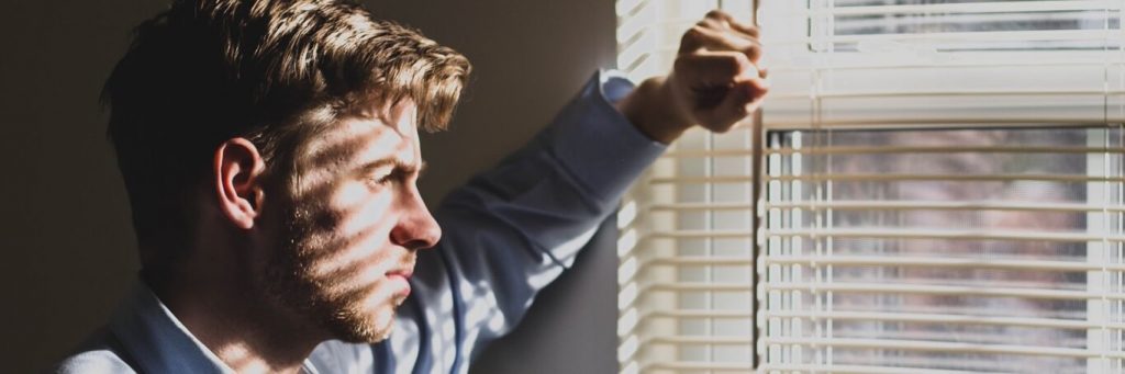 man stood beside window thinking worrying
