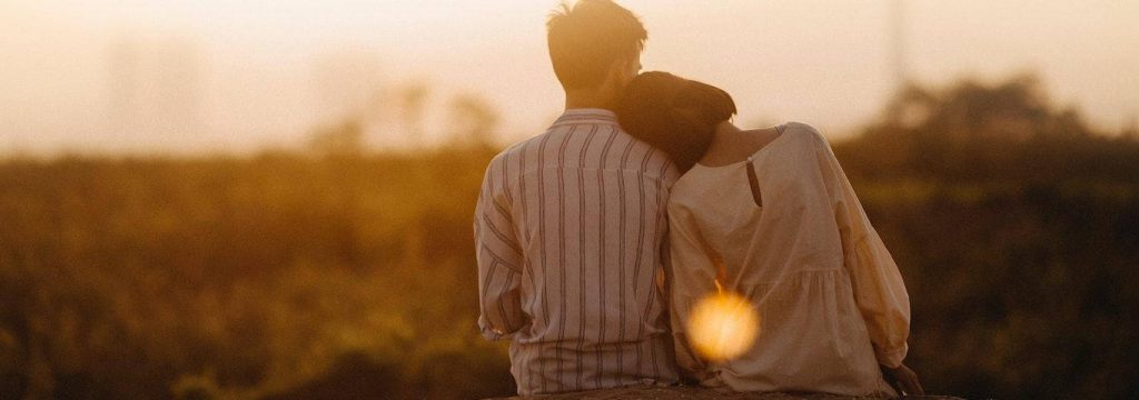 couple sits watching sunset while woman lying on partner shoulder