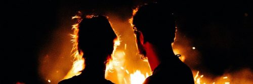 man facing backward looks at girlfriend near flame