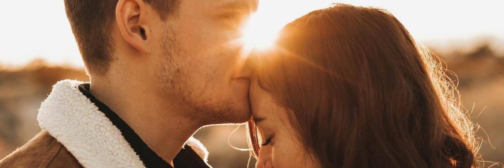 man kissing girlfriend forehead in sunny sky
