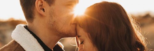 man kissing girlfriend forehead in sunny sky