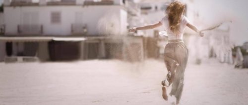 woman facing backward runs on sandy dusty street