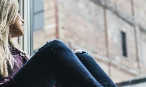 woman sits next to window looking at tall old building