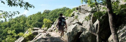 man wearing back bad climbs rock in beautiful blue clear sky