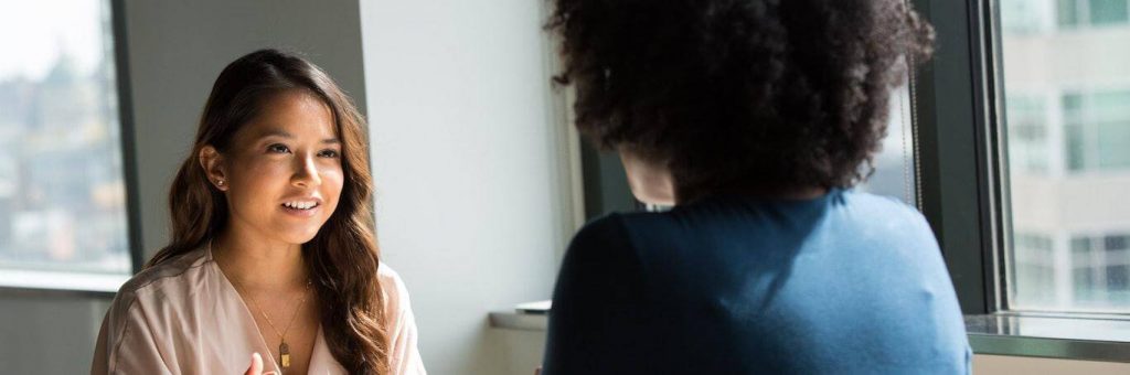 woman happily talks discussed with curly hair woman in office