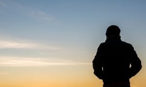 man shadow stands facing backward looking at red blue partially clear sky