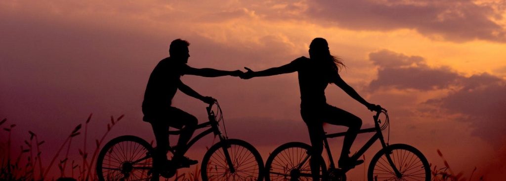 couple shadow rides two bikes hand in hand in beautiful sunset