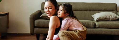 woman carries adorable daughter smiles sitting beside couch in living room