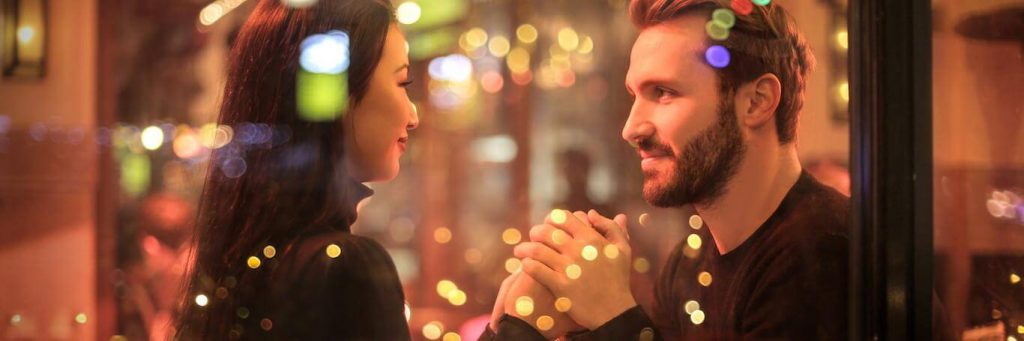 couple sits in coffee shop holding hands looking happily at each other