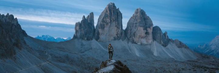 person stands on rock looking hills in blue clear sky