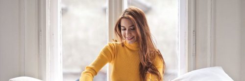 woman sits beside window in bed happily smiling