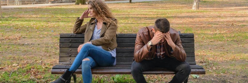 couple sits on bench having conflict while man hands in face upset