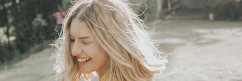 short blonde hair woman stands on beach happily smiling