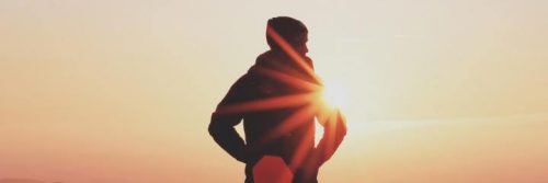 man facing backward stands hand in pock in sunset sky