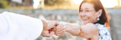 elderly woman happily smiles holding husband hand
