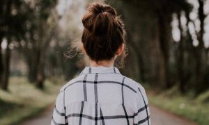woman facing backward stands on road between forest