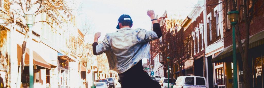 man dances on street facing backward in vibrant busy city