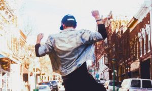 man dances on street facing backward in vibrant busy city