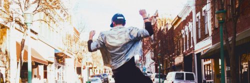 man dances on street facing backward in vibrant busy city