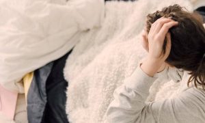 girl sits on bed touching hair warming up with white blanket