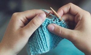 two hands holding needle knitting blue wool