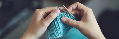 two hands holding needle knitting blue wool