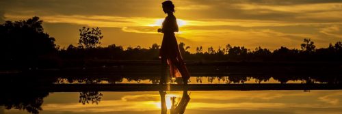 woman walks alone along lake in sunset dark sky